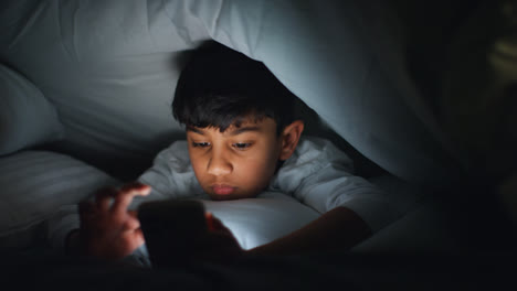 Close-Up-Of-Young-Boy-In-Bedroom-At-Home-Using-Mobile-Phone-To-Text-Message-Under-Covers-Or-Duvet-At-Night-9